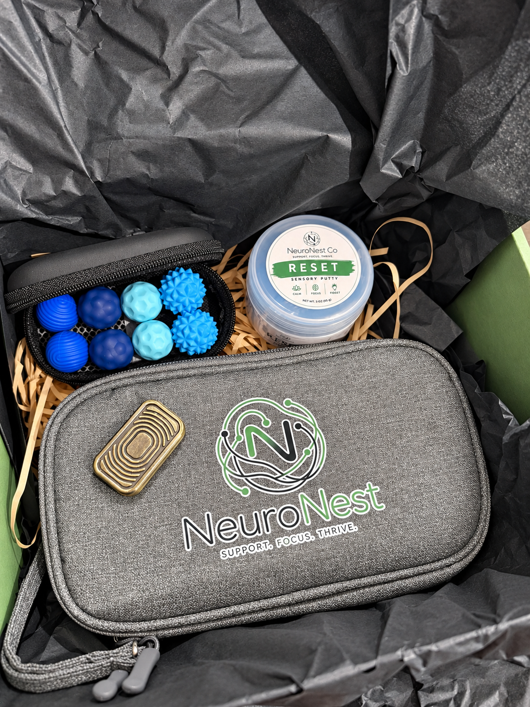 Completed NeuroNest adult fidget gift box with one brass-look slider, one Reset Putty container, eight blue magnetic balls and one gray organizer