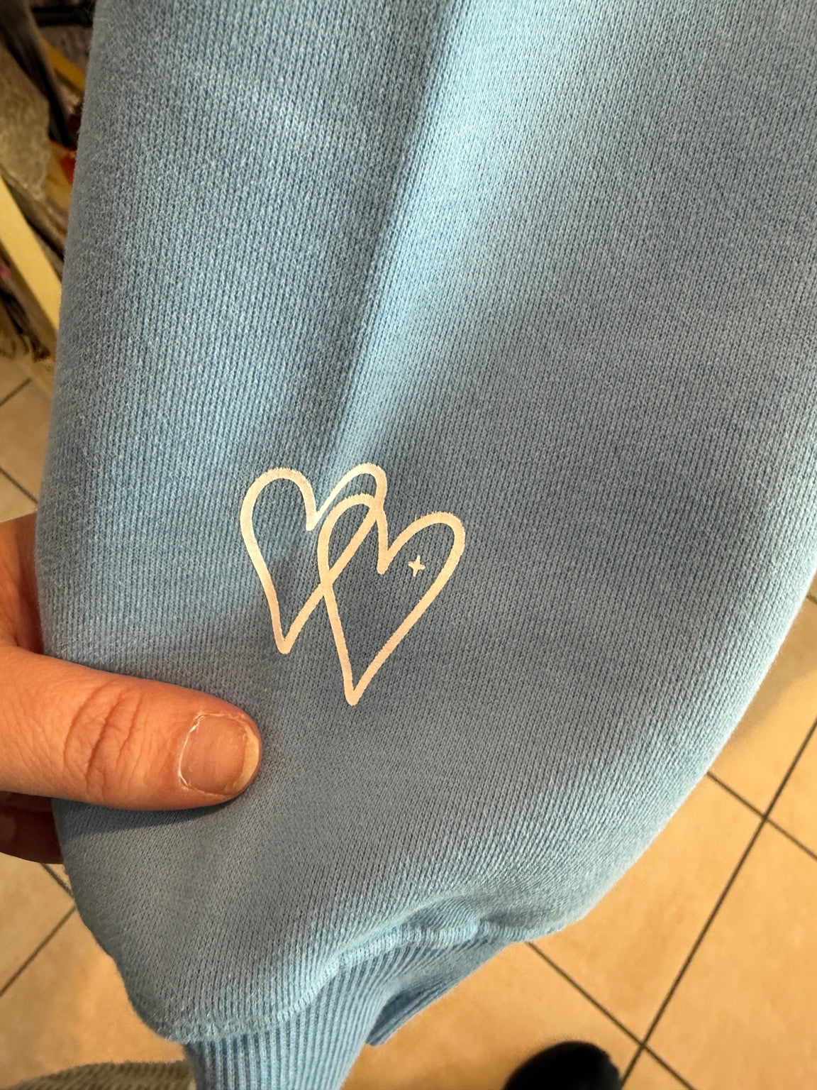 Interlocking heart graphics at the wrist of the light-blue LOVED. hoodie